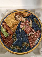Close-up of the round decorative plate showing mosaic art style woman in detailed colors with signature visible.