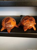 Shows two carved wooden turtle boxes side by side on a shelf, highlighting their shape, wood tone and carved details.