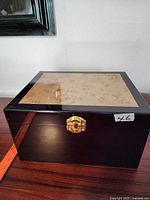 Front view of the large dark wood jewelry box with gold tone clasp and burl wood veneer top.