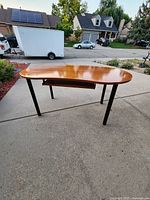Side angle view of a large bean-shaped wooden desk showing black metal legs and underside keyboard tray, highlighting the smooth wood finish and leg design.