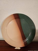 Large round ceramic plate showing horizontal stripes of cream, brown, and green colors on top surface.