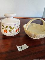 Side view of sugar container with fruit and flower design next to Lenox dish.
