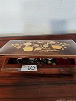 Partially open wooden jewelry box with floral inlay on lid, showing glimpse of jewelry inside