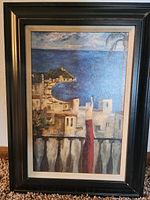 Framed oil painting showing a coastal town with buildings and the sea at the horizon.