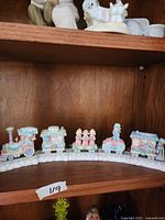 Full view of all six separate Precious Moments Christmas train cars arranged on a white snowy track base on a wooden shelf.