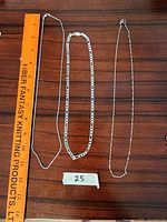 Three silver chains laid flat on wooden surface alongside ruler for length measurement