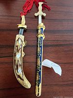 Two small cloisonné replica swords placed side by side on a wooden surface, showing detail of the sheaths and handles.