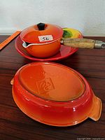 Vintage orange enamel cooking pot with wooden handle, glass lid, and matching trivet