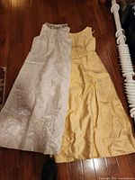 Two full-length vintage formal dresses lying flat, one yellow and one light beige with embossed floral pattern and jeweled neckline.