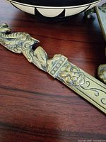 Close-up of decorative brass knife with intricate lion and floral motif design, showing patina and wear.
