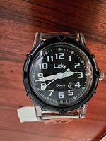 Front view of the watch face showing black dial, white numerals and Lucky brand logo.