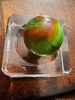 Top view showing colorful swirled marble sitting in a clear rectangular stand on a wooden surface