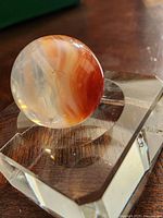 Close-up photo of the vintage glass marble showing orange and white swirling pattern inside the transparent glass.