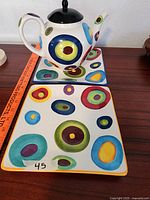 Photo of teapot placed on one of the colorful square plates showing the pattern and size.