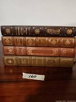 All four vintage hardcover books stacked horizontally, showing spines with gold embossed titles and decorations.