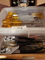 Vintage Steadfast screwdrivers with yellow amber handles, additional screwdrivers, and pliers with black handles laid out in a plastic bin.
