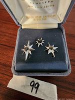 Photo of three-piece set: a pin and two cufflinks, each featuring a black star sapphire stone set in sterling silver starburst design, displayed in a velvet jewelry box.