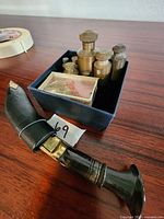 Photo showing the brass scale weights set in a blue box alongside the sword letter opener with the black handle in focus.