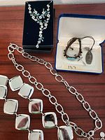 Photo showing two silver-tone chain belts, one being a vintage Talbots belt with interlocking links and another with large smooth square links, along with a floral rhinestone necklace and matching earrings on black velvet background and a small blue velvet case with leather bracelet and religious medal pendant.