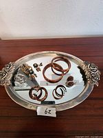 Top view of silver oval tray with mirrored surface holding various jewelry including wooden bangles, hoop earrings, and clip-on earrings.