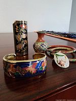 Photo showing three cloisonné bracelets, a petite multicolored cloisonné vase, cloisonné lighter holder with black background, and one petal-shaped cloisonné earring with floral design.