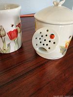 Photo showing the ceramic music box watering can with floral tulip and butterfly decorations and a ladybug detail, alongside the matching floral mug.