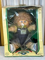 Front view of the 14-inch Cabbage Patch Kids doll seated inside the original cardboard box with visible wear and torn plastic window.