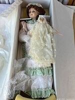 Porcelain doll in original box, showing pastel green lace dress and baby doll companion wrapped in lace fabric and bubble wrap.