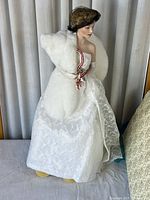 Porcelain doll dressed in white lace Victorian style dress with white fur stole and brown hat