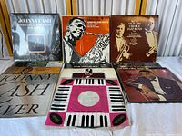 Photo of vinyl records lined up with visible titles on album covers including Johnny Cash, Gerry Mulligan Tentette, King Oliver's Creole Jazz Band, Nat King Cole and others. Shows condition of covers and packaging.