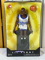Full view of Li'l Penny figure in original yellow and black packaging with mini basketball accessory visible. Packaging corners show wear and aging.