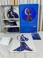 Full view of the Barbie doll in original box with the signed fashion illustration, doll stand, and other included documentation laid out in front