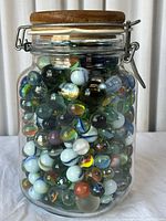 Front view of glass jar filled with colorful glass marbles, wooden lid on top, metal clasp visible.