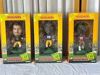 Three NFL Headliners XL collectible figures in original yellow Headliners boxes with protective windows. Figures depict Grbac (#15), Martin (#29), and Dunn (#28) in NFL uniforms holding footballs.