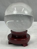 Crystal ball displayed on wood stand, showing clear, polished surface with light reflections.