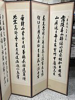 Full view of the 8-panel folding privacy screen showing hand painted Chinese calligraphy on all panels.