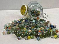 Hexagonal jar tipped on its side with many marbles spilled out showing size and color variety.