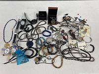 Wide photo showing large assortment of different costume jewelry items spread out, including multiple beaded bracelets and necklaces, two watches, some pendants, and boxed pieces.