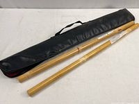 Two 26-inch bamboo sticks with natural finish placed next to black padded zippered carrying case with carrying handle.