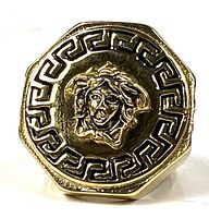 Front view of gold tone men’s ring with raised Medusa head emblem surrounded by Greek key pattern in black enamel.