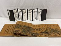 Wide shot showing the 8-panel folding screen open behind the long illustrated accordion-style book stretched out in front.