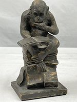 Front view of cast metal sculpture showing monkey reading a book while seated on books.