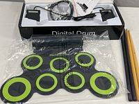 Digital drum pad set with 7 black and green circular pads, packaged with other kit components including drumsticks and cables inside original box