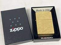 Top view of brass Zippo lighter in original box with black Zippo-branded lid to the side.
