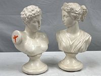 Pair of white plaster neo-classical busts of a man and woman on rounded pedestals with slight scuffs. Male bust marked with red on left shoulder, female bust in classical draped robe.