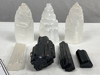 Front view of all 7 specimens showing 3 large selenite crystals, 1 smaller selenite piece, and 3 black tourmaline crystals of varying sizes on a white surface.