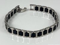 Full view of bracelet showing the open clasp, circular stainless steel links with black insets, and the length of the bracelet on a white reflective surface.