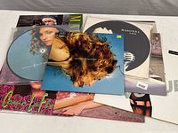 Photo showing multiple vinyl records and singles in their covers laid out on a surface, including Madonna's 'Ray of Light' and other titles.