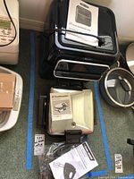 Bella black air fryer dehydrator oven with manual on top, Toastmaster chrome waffle baker, Black and Decker mixer accessories in plastic bag alongside.