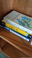 Photo of three stacked bird field guide books on a wooden surface.
